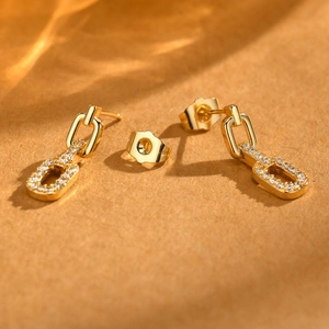 Close-up of gold chain earrings with zircon pendants on textured brown background