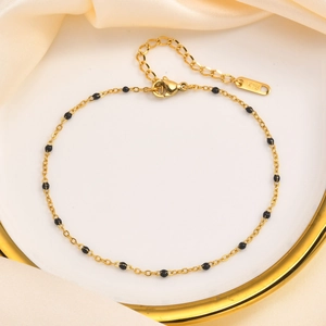 Elegant gold stainless steel anklet with black beads and K18 hallmark on silk background
