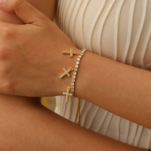 Detailed close-up of golden cross charm bracelet with sparkling zircon stones and adjustable clasp