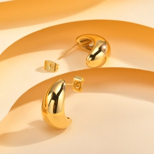 Detail of gold teardrop earrings with high-polish finish on a minimalist geometric background