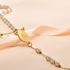 Detailaufnahme eines goldenen Maria-Anhängers an einer weißen Perlen-Rosenkranzkette