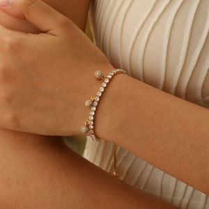 Close-up of gold tennis bracelet with white zircon stones and three pave ball pendants
