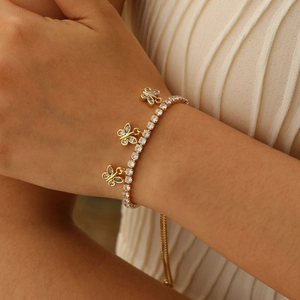 Detail view of a gold-plated butterfly charm bracelet with square zircon stones on wrist