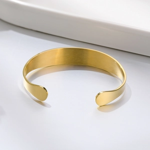 Detail of a polished gold stainless steel medical cuff bracelet on a white tray