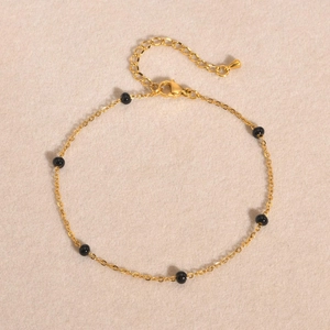 Détail d'une chaîne en acier doré avec des perles noires polies et un fermoir mousqueton