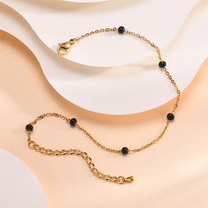 Chevillère dorée en acier inoxydable avec perles noires sur fond artistique épuré