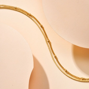 Detailed macro view of 18K gold double-layered snake chain and beaded anklet texture