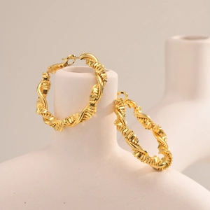 Polished golden spiral twist hoop earrings displayed on a minimalist ceramic holder