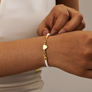 Adjustable white woven rope bracelet with gold heart charm and beads on woman's wrist