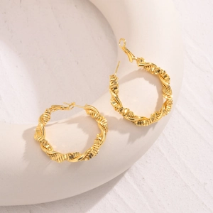 Macro detail of golden spiral twisted hoop earrings on a white decorative stone pedestal