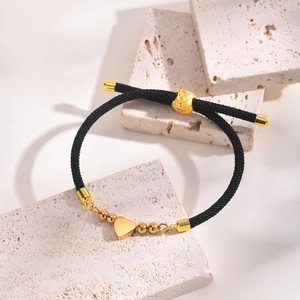 Detail of adjustable black woven bracelet with gold heart charm on travertine stone