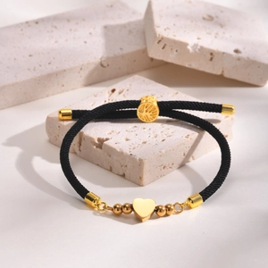 Detail of black woven cord bracelet with gold heart pendant and tree pattern charm