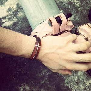 Men's stainless steel and rosewood cross bracelet on a leather strap in a cool industrial setting