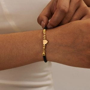 Adjustable black woven rope bracelet with gold heart charm and beads on woman's wrist