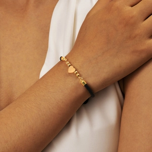 Macro shot of an adjustable black cord bracelet with a gold heart pendant and round beads