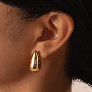 Close-up of golden teardrop earring with high-polish metallic finish on model ear