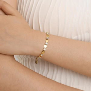 Gros plan d'un bracelet en or 18 carats avec zircon et motifs cœurs sur un poignet féminin
