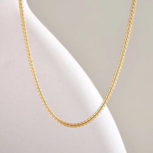 Gros plan d'un collier en acier inoxydable doré tressé sur un support d'exposition