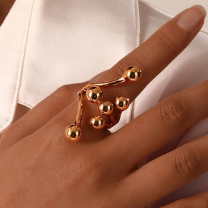 Détail d'une bague dorée artistique avec cinq sphères polies portée sur l'index féminin