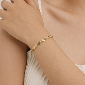 Détail d'un bracelet à maillons en forme de cœur doré avec zircons brillants au poignet