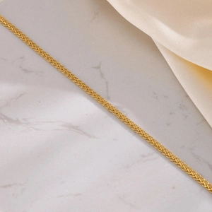 Détail d'un collier chaîne tressée en acier inoxydable doré sur marbre et soie