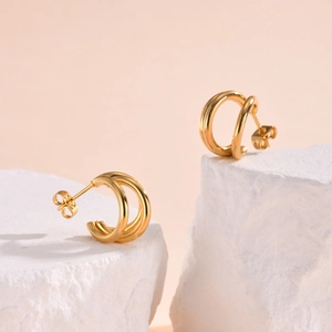 Detail shot of golden C-shaped triple-layer earrings on elegant white stone display