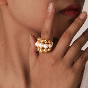 Macro detail of layered gold ball ring with faux pearls on model's finger