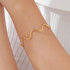 Detail of elegant gold wave-shaped arm cuff on model highlighting shiny metal texture