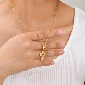 Detailed close-up of a golden religious cross pendant necklace worn on a white knit sweater