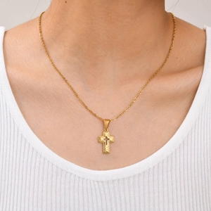 Close-up of gold stainless steel cross necklace with baroque relief on a white knit shirt