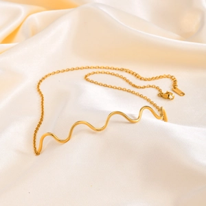 Close-up of golden wavy bar pendant on elegant silk background with soft drapes