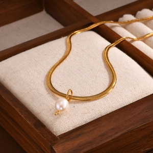 Elegante goldene Schlangenkette mit einer runden weißen Perle auf einer Holzbox
