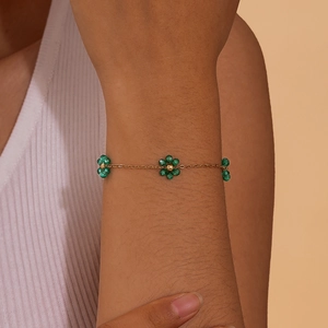 Close-up of a gold floral bracelet with green beaded flowers on a woman's wrist