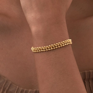Close-up of a three-strand gold beaded bracelet on a woman wrist with polished finish