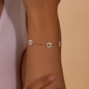Close-up of golden bracelet with white pearl flower charms worn on a wrist