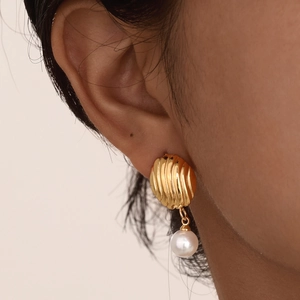 Close-up of gold shell texture earrings with elegant white round pearl pendants
