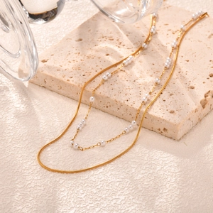 Elegant gold double layer necklace with snake chain and small pearls on stone surface