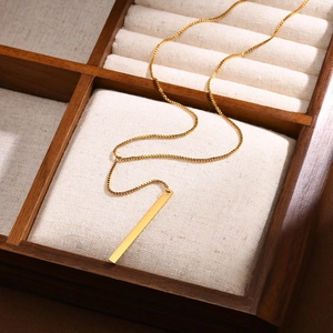Collier en Y doré avec chaîne vénitienne et pendentif barre sur plateau à bijoux en bois