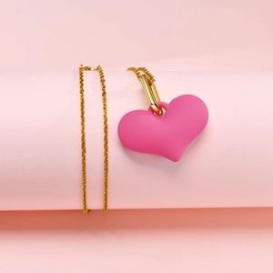 Gros plan d'un pendentif cœur rose mat sur une chaîne dorée sur fond rose pastel délicat