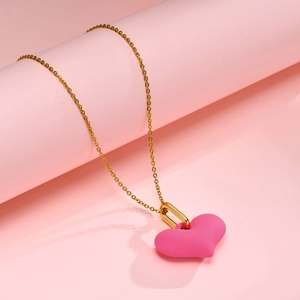 Détail d'un pendentif cœur rose avec chaîne dorée sur fond rose pastel doux