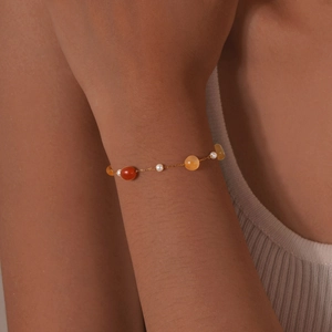 Detail of a thin gold chain bracelet with pearls and carnelian beads on a wrist