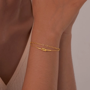 Detail of gold double-layered knotted chain bracelet worn on female wrist with knit sweater