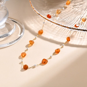 Detailed shot of golden chain necklace with amber, dark beads and pearls on glass