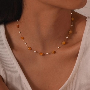 Detailed view of amber beads and white pearls on a gold chain necklace worn by a model