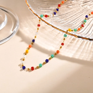 Detail of colorful cube bead necklace with 18K gold chain on textured glass tray