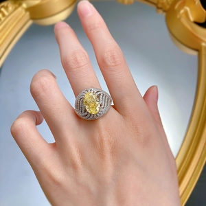 Dettaglio di un anello con gemma gialla ovale e intricata lavorazione in pavé di diamanti