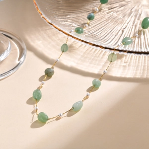Close-up of green jade beads and white pearls on a gold chain with soft shadows