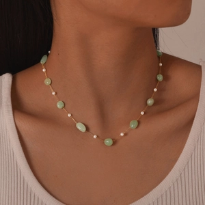 Close-up of a gold chain necklace with green jade beads and white mini pearls on a model