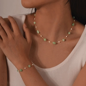 Golden chain jewelry set with green stones and pearls worn by a model in knitwear