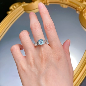 Macro detail of a rectangular light blue gemstone ring with pave diamonds on the hand